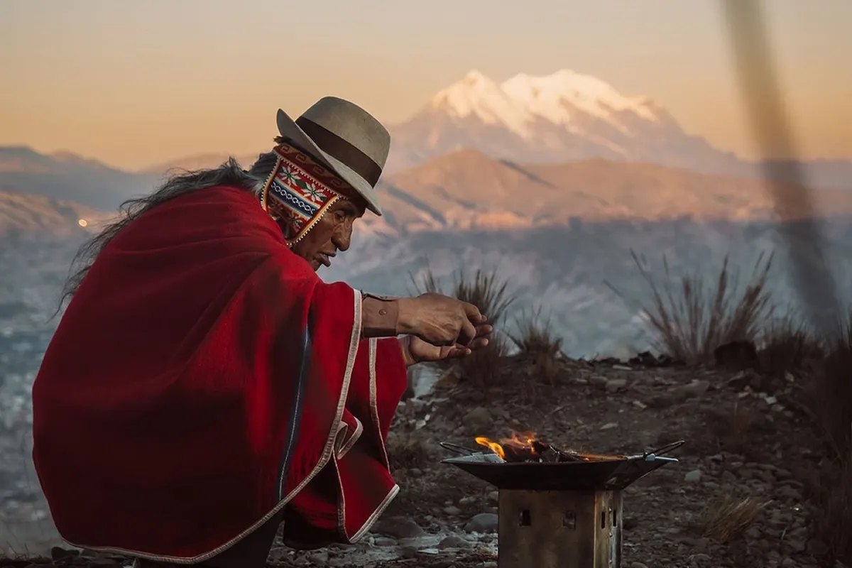 A man in a red poncho and hat at a viewpoint above La Paz, the snow-covered Illimani behind him at sunset