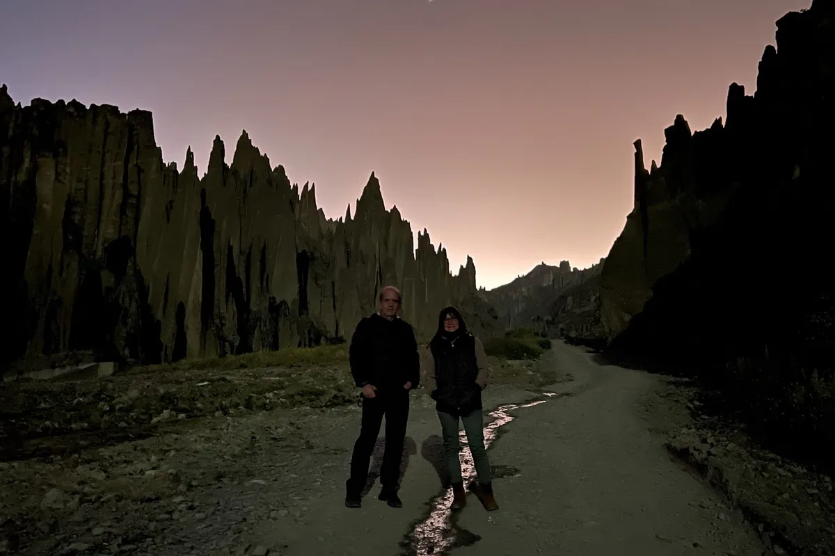 Two travelers walking into Valle de las Ánimas before sunrise, the spires dark against a pale sky