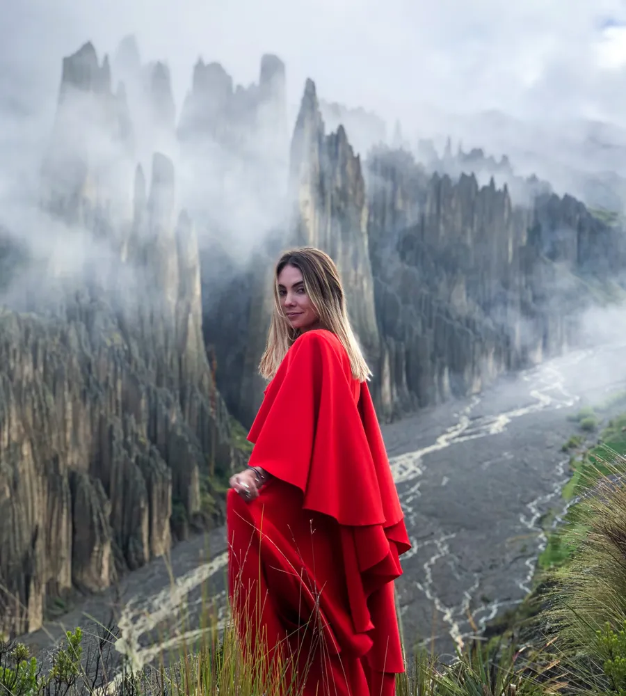 A traveler in a red dress on the ridge of Valle de las Ánimas, spires and clouds behind