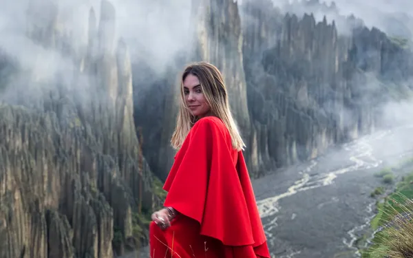 A traveler in a red dress on the ridge of Valle de las Ánimas, spires and clouds behind