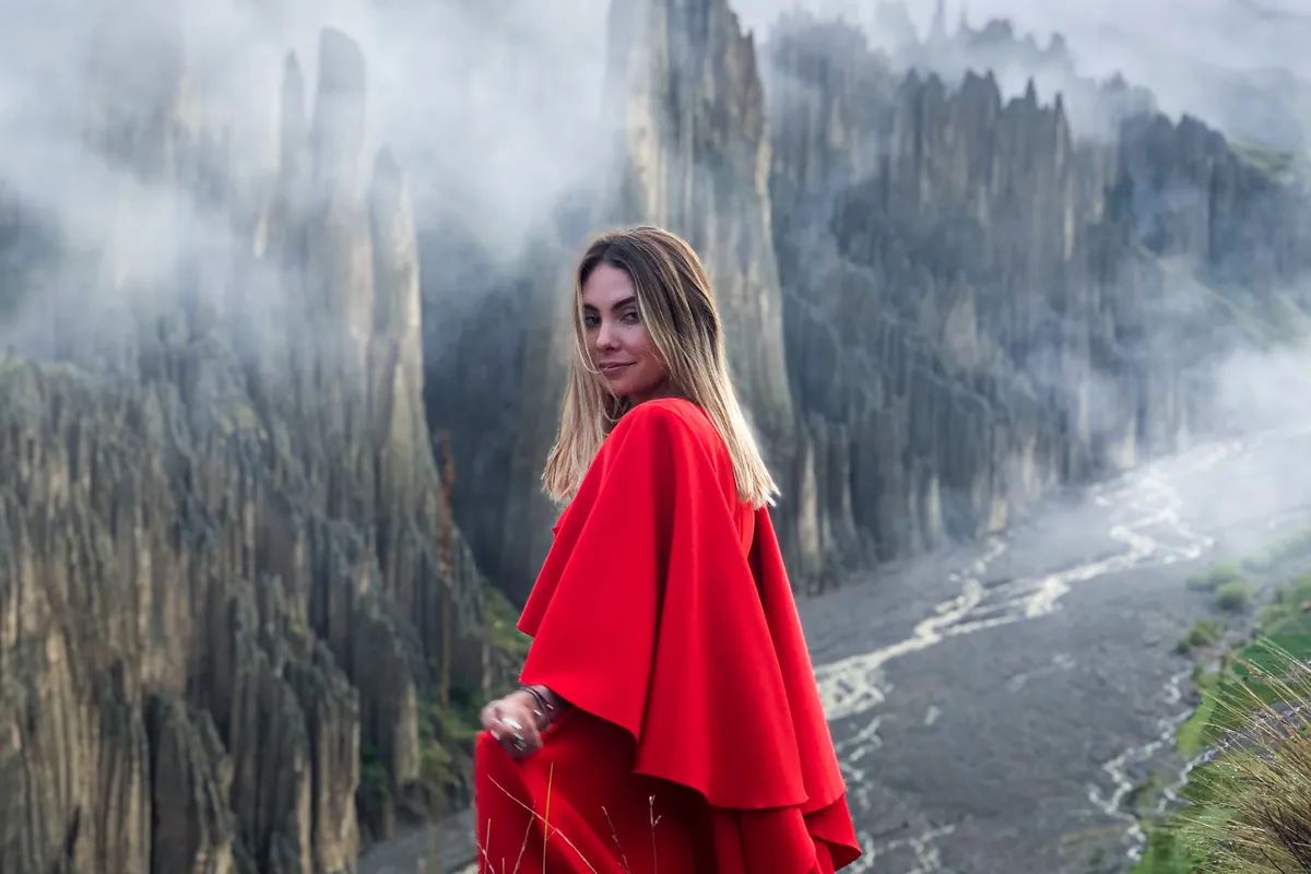 A traveler in a red dress on the ridge of Valle de las Ánimas, stone spires and clouds behind, the dry riverbed below