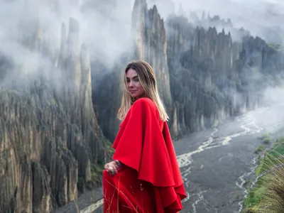 A traveler in a red dress on the ridge at first light, clouds between the spires