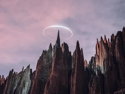 The spires at dusk under a pink sky, a ring of light above the tallest one